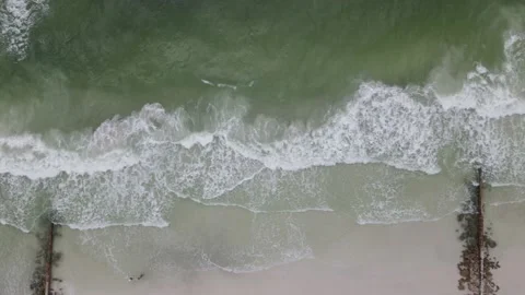 Top down aerial drone shot of waves on a beach passing by jetty and dock 4k h Stock Footage 139216229