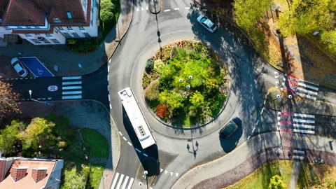 Top-down aerial drone shot of a white bus and car navigating a city roundabout Stockbeeldmateriaal 320919673
