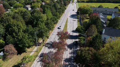 Top-down aerial drone shot of a car driving along a tree-lined suburban road. EV Stock Footage 321115946