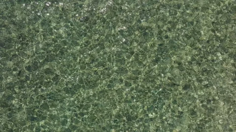 Top-down aerial drone view of gentle sea waves washing onto a pebble beach in Stock-Footage 346891455