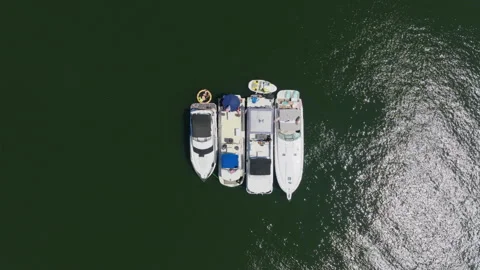 Top-down aerial drone view of four boats rafted together on a dark green lake Stock-Footage 347673714