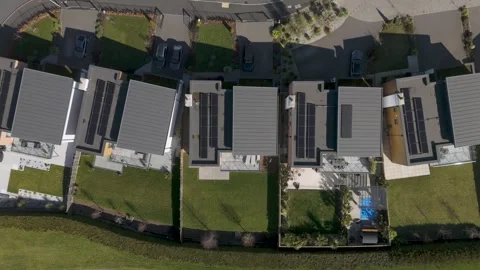 Top-down aerial of mirrored plots of dark-roof solar homes with fenced gardens Stock Footage 310600296