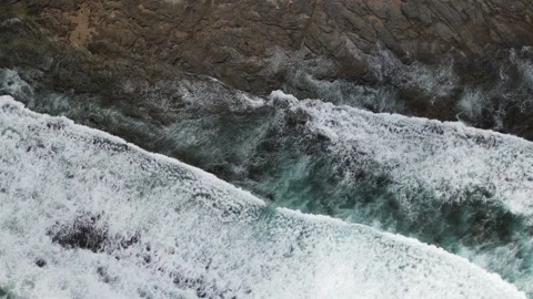 Top down aerial of ocean waves on dark rocky shore Stock Footage 336005513