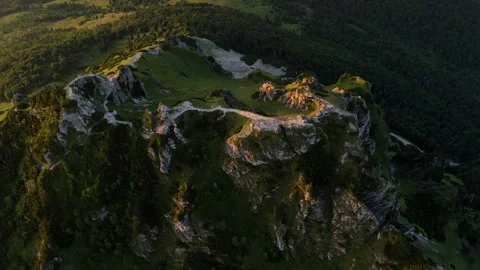 Top-down aerial orbit of rocky mountain peak with greenery at sunrise Stock-Footage 315445694