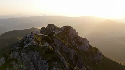 Top-down aerial orbit of rocky mountain peak with greenery at sunrise Stock Footage 317238427
