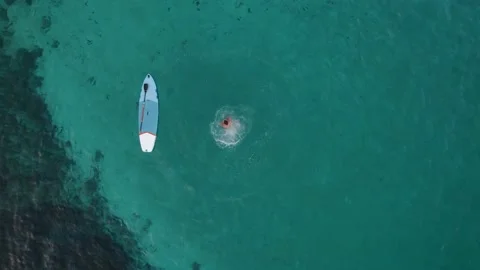 Top down aerial shot of man jumping from his paddle board in crystal clear tu 스톡 동영상 154906751