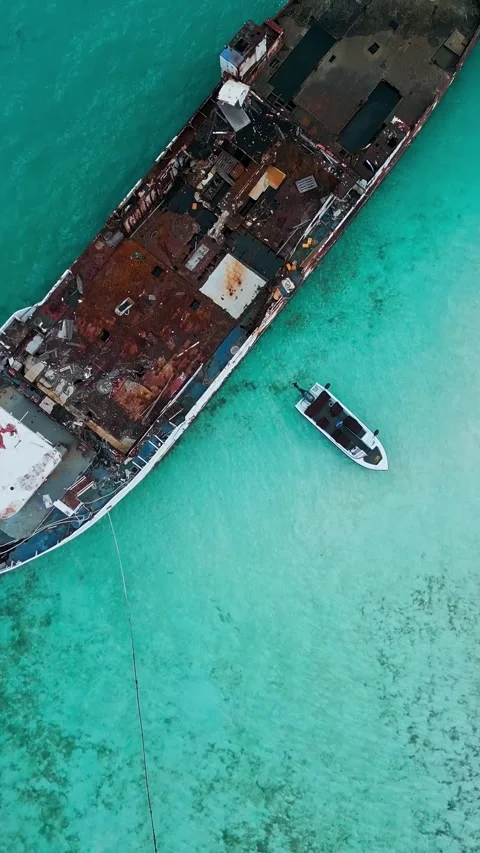 Top down aerial shot of small boat near giant rusty shipwreck in clear ocean Vídeo Stock 347397844