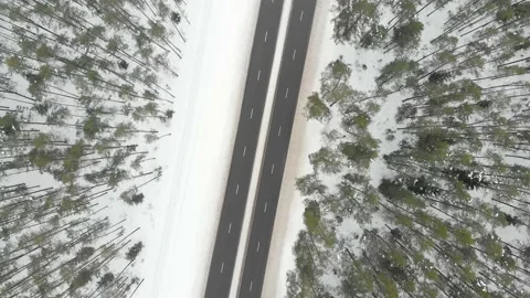Top down aerial spinning view of snow covered forest with a two-lane road 스톡 동영상 227068401