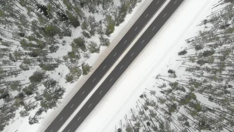 Top down aerial spinning view of snow covered forest with a two-lane road 스톡 동영상 245871822
