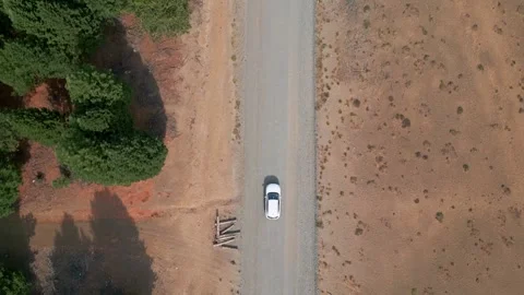 Top down aerial tracking shot of car driving on dirt road through arid terrain Видео 331160256