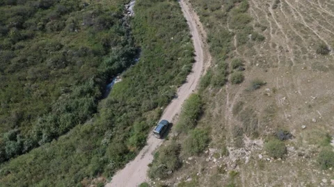 Top-down aerial tracking shot of 4x4 on dirt road beside a stream, Kyrgyzstan Видео 347239960