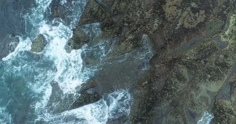 Top down aerial video of waves crashing on dark coastal rocks The Raw Power.. Video stock 316643260