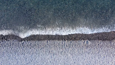 Top down aerial view above layered white sand and pebble beach washed over Stock Footage 234617035
