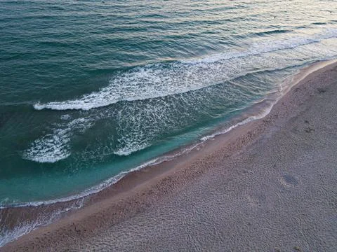 Top down aerial view of beach with waves crashing into the sand during evening Stock Photos