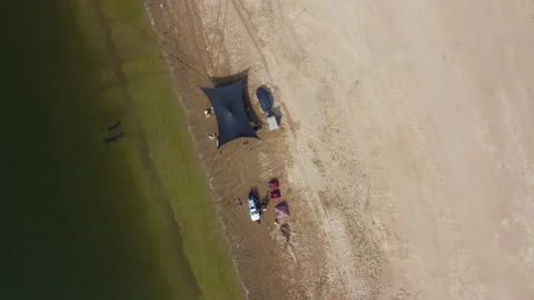 Top down aerial view of campsite with black tent and 4x4 cars on sandy bank Stock Footage 335080047