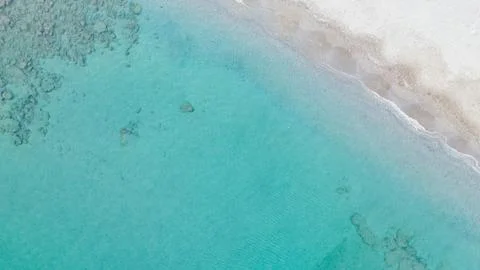 Top down aerial view of clear turquoise sea water meeting light sandy beach.. Stockfoto's