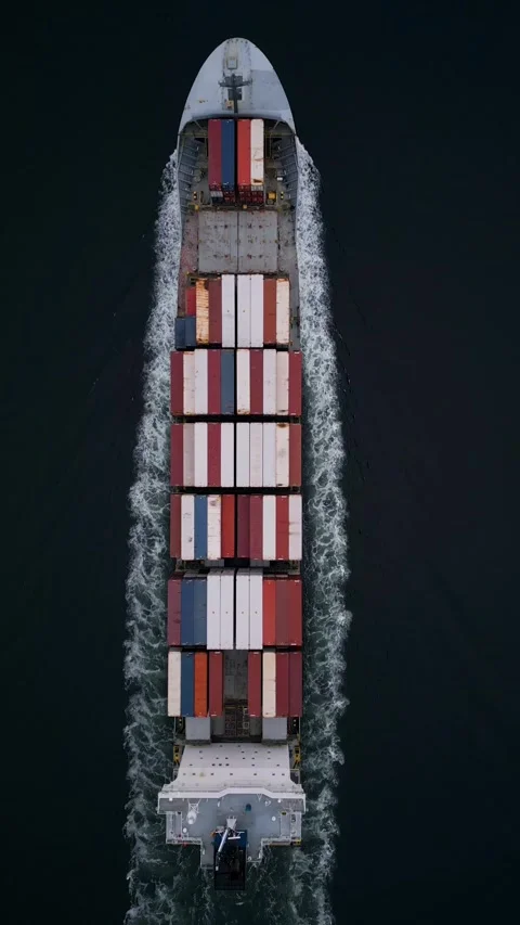Top-down aerial view of container ship cutting through dark water, leaving white 库存影片 325741120