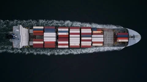 Top-down aerial view of container ship cutting through dark water, leaving white Video stock 325741150