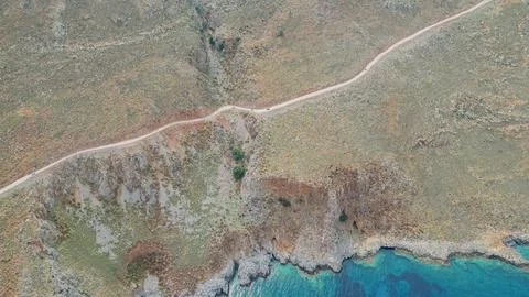 Top down aerial view of dirt road with driving cars along rocky coast and b.. Stock Photos