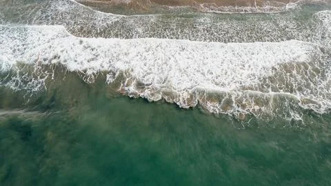 Top down aerial view of emerald sea waves washing ashore with white foam on.. Stock Photos