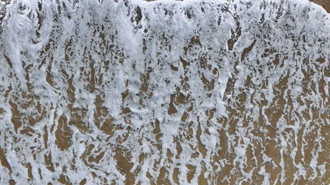 Top down aerial view of foamy waves washing onto sandy beach Stock Footage 339777801