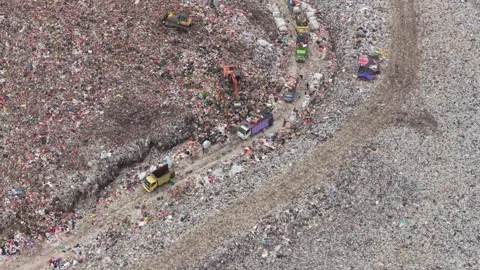 Top down aerial view of heavy machinery and queues of garbage trucks dumping Stock Footage 328480419