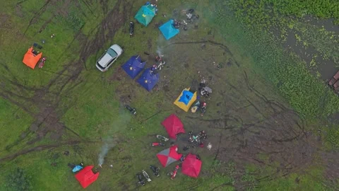 Top down aerial view of a large group camping in a grassy field next to a lake 動画素材 331090399