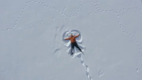 Top-down aerial view of a middle-aged man making a snow angel in fresh snow Stock Footage 148755689
