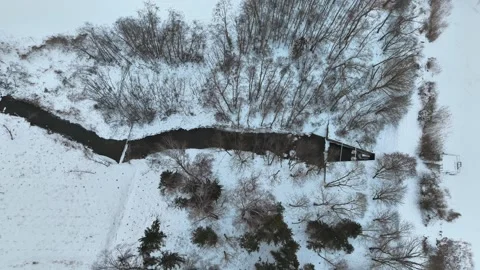 Top-down aerial view of a narrow river forming a small frozen pond with a Vídeo Stock 331610874