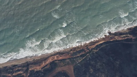A top-down aerial view of ocean waves splashing against the rocky shore on the Stock Footage 168168801