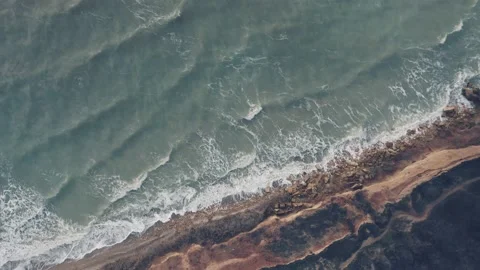 A top-down aerial view of ocean waves breaking against the rocky shore on the Stock Footage 168168812