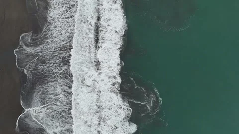 Top down aerial view of ocean waves breaking on black sand beach Video stock 337915042