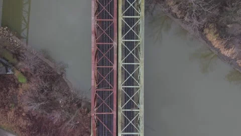 A top-down aerial view of parallel railway bridges crossing a calm river Stock Footage 328707783
