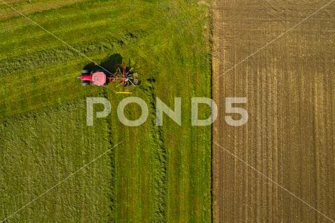 Top down aerial view of a red tractor cultivating farmland with a spinning rack Stock Photos