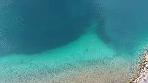 Top down aerial view rising from turquoise lake water revealing shoreline 스톡 동영상 329506106