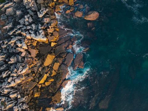 Top down aerial view of rugged rocky shoreline with waves crashing into sto.. Stock Photos