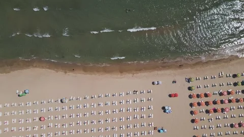 Top-down aerial view of a sandy beach with rows of umbrellas and sunbeds, gentle Stock Footage 316837738