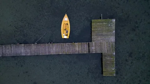 Top-down aerial view of small yellow boat moored at wooden pier over clear water 库存影片 325741286