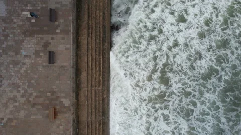 Top down aerial view of storm waves crashing against a concrete barrier seawall Stock Footage 221130027