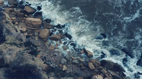 A top-down aerial view of storm wind rolling waves over rocky ocean coast Video stock 237461478