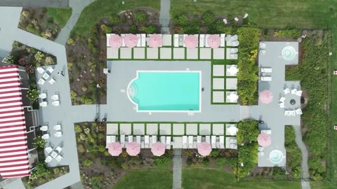 Top-down aerial view of a stylish hotel pool with red-striped umbrellas, lounge Vidéo 310187215