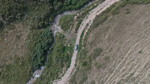 Top-down aerial view of an SUV on a dirt road by a stream, Kyrgyzstan Видео 347239972