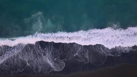 Top down aerial view of turquoise ocean waves crashing on a black sand beach Video stock 335760221