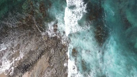 Top down aerial view of turquoise ocean waves washing over rocky shore and sandy Stock Footage 335984800