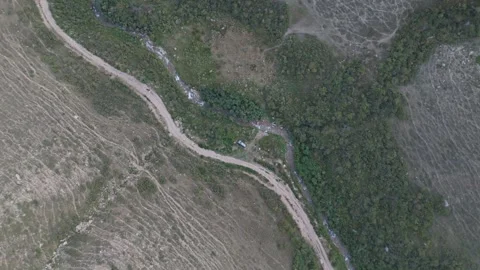 Top-down aerial view of a winding dirt road beside a stream, Kyrgyzstan Видео 347240153