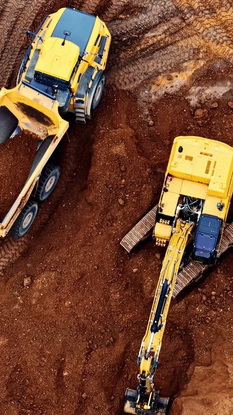 Top-down aerial view of a yellow excavator digging and loading a large dump Stock Footage 346586563