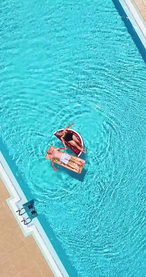 Top-down aerial view of a young couple relaxing and sunbathing on inflatable Stock Footage 344820568