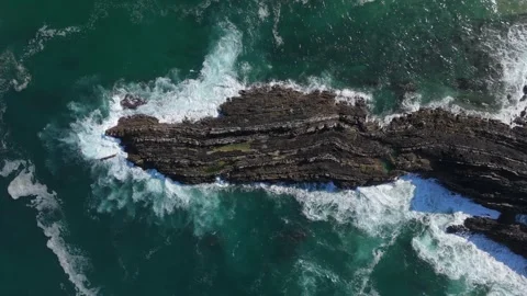 Top-down aerial of waves crashing around a rock reef in turquoise sea, Portugal Stock Footage 346377511