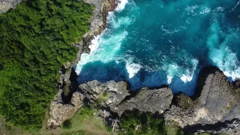 Top down aerial zoom out showing powerful waves hitting rugged cliff Видео 320790028