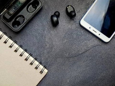 Top-down composition featuring a spiral-bound notebook, cordless earbuds, a.. Stock Photos